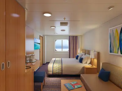 Ansicht einer hellen, modernen Außenkabine der Carnival Horizon mit Doppelbett, Sofa, Fenster mit Meerblick und Surfbrett-Kunst.