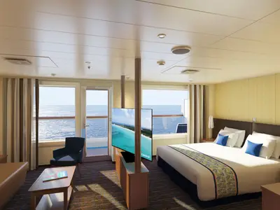 Geräumige Balkonkabine auf der Carnival Horizon mit Doppelbett, Sitzbereich, Flachbild-TV und Balkon mit Meerblick.
