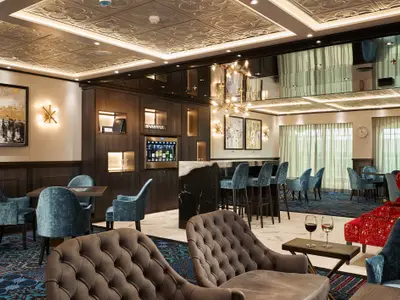 Blick in eine elegante Bar-Lounge mit weichen Samtsesseln, einem Weindispenser, einem Marmortresen und modernen Kunstwerken. Zwei Weingläser stehen auf einem Tisch im Vordergrund.