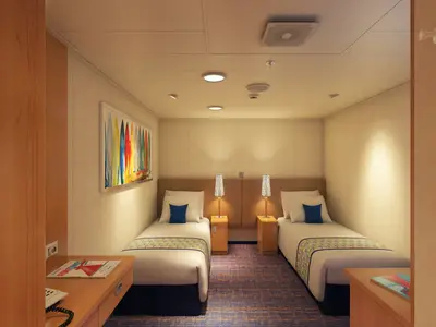Eine moderne, helle Innenkabine auf der Carnival Horizon mit zwei getrennten Einzelbetten, Nachttischen und Lampen. Eine lange, bunte Grafik an der Wand zeigt Surfbretter. Ein Schreibtisch mit Magazin befindet sich links im Vordergrund.