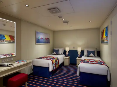 Innenansicht einer modernen Kabine der Carnival Horizon mit zwei Einzelbetten, Schreibtisch und Spiegel. Nautisches Dekor mit blauen Akzenten und Segelboot-Bildern. Gestreifter Teppich und Nachttische.