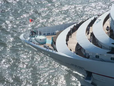 Vogelperspektive auf das Vorderteil der Carnival Horizon. Passagiere stehen auf mehreren offenen Decks und blicken auf das sonnenbeschienene, glitzernde Meer.