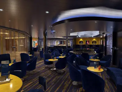 Innenansicht einer eleganten Schiffsbar mit dunkelblauem Dekor. Zahlreiche Samtsessel und gelbe Tische sind auf einem gestreiften Teppichboden arrangiert. Eine geschwungene Bar und künstlerische Wandelemente sind im Hintergrund sichtbar. Cocktails stehen auf den Tischen.