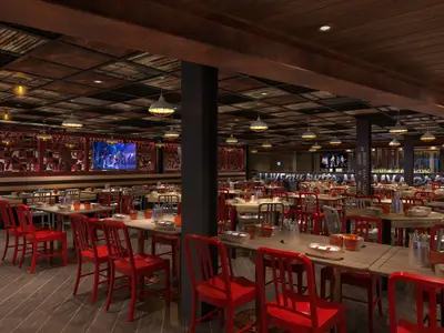 Weitwinkelansicht eines großen, modernen Restaurants mit vielen leeren Holztischen und roten Stühlen, beleuchteten Bildschirmen und einer Bar im Hintergrund. Industrial-chic Design mit Holzböden und Metall-Deckendekor.