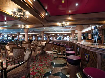 Geräumiges Casino der Carnival Legend mit langer Bar, vielen Tischen, Stühlen und Reihen von Slot-Maschinen. Eine Ritterrüstung steht an der Bar.