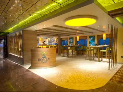 Modernes Bonsai Sushi Restaurant an Bord. Holztische mit grünen Barhockern, eine Theke. Gelbe Deckenlampe, Bambus-Deko und hellem Mosaikboden.