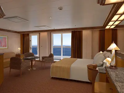 Innenansicht einer geräumigen, eleganten Suite auf der Carnival Legend mit Doppelbett, Sitzbereich, Balkon zum Meer und Bartheke.