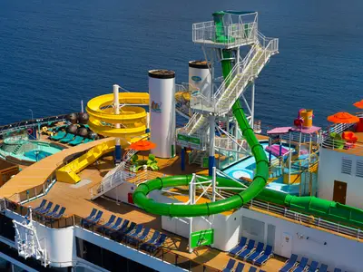 Sonnendeck auf der Carnival Legend mit Wasserpark: bunte Wasserrutschen, Pools, Liegen und Schirme. Im Hintergrund das weite blaue Meer.