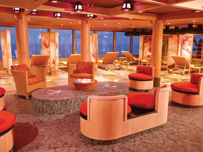 Ein heller Innenraum einer Spa-Lounge auf der Carnival Luminosa mit großen Fenstern zum Meer, Holzvertäfelung und orangefarbenen Möbeln zum Entspannen.