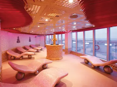 Heller Spa-Wellnessbereich auf der Carnival Luminosa. Pinke Mosaik-Liegen, große Fenster mit Meerblick und rote Deckenakzente.