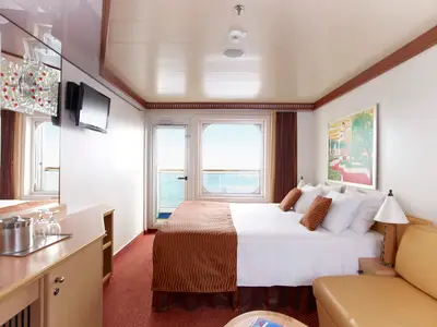 Helle Balkonkabine auf der Carnival Magic. Ein großes Bett, Fenster und Tür mit Meerblick. Flachbildfernseher und Beistelltisch mit Gläsern sind sichtbar.