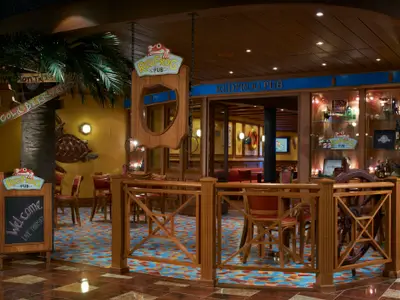 Thematisierte RedFrog Pub Bar auf der Carnival Magic. Tropische Atmosphäre mit Palme, Holzmöbeln und maritimem Dekor. Eine Tafel 'Welcome Live Thirsty'.