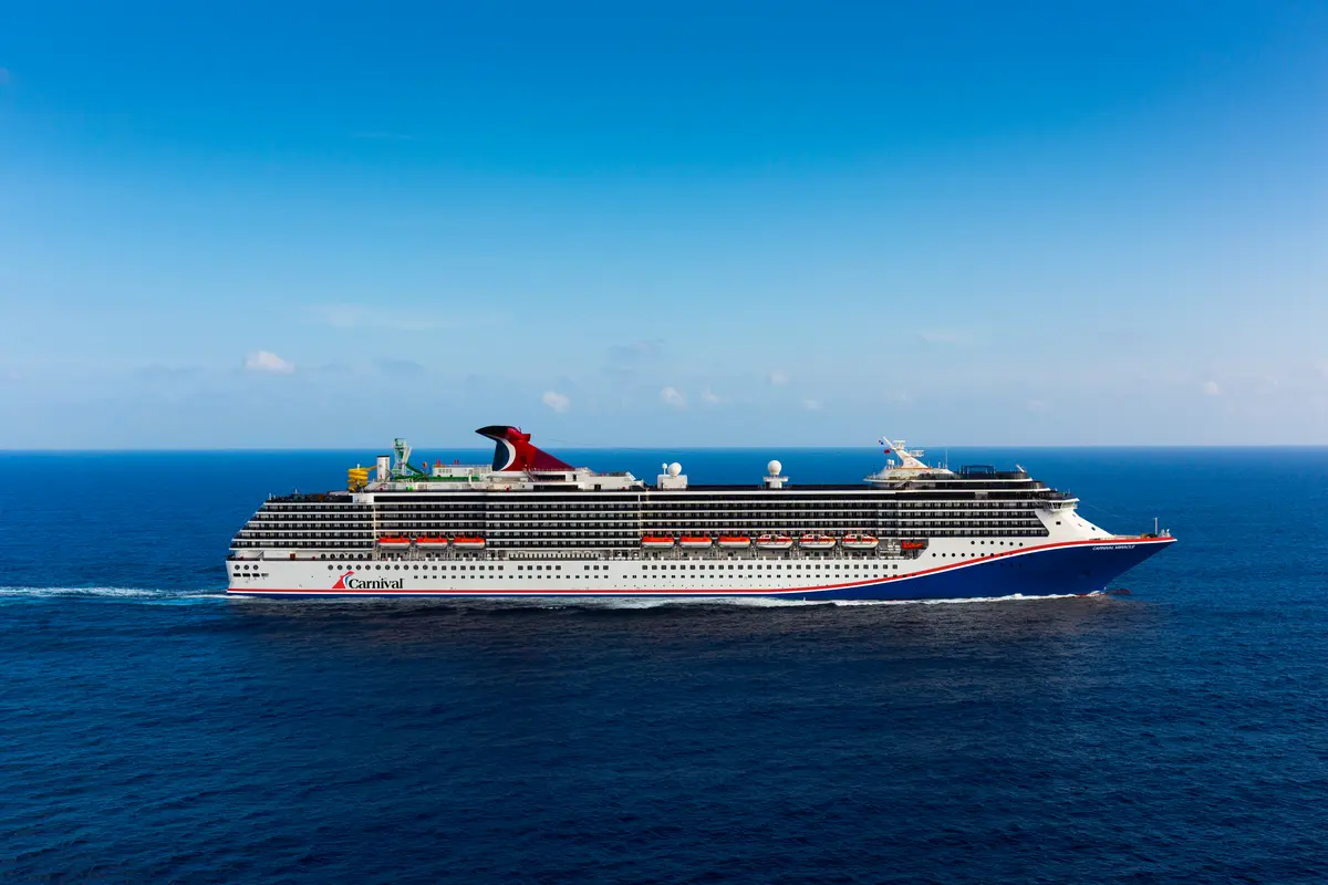 Ein großes, weiß-blaues Carnival Miracle mit rotem Schornstein auf offener See. Der blaue Himmel ist nur leicht bewölkt.
