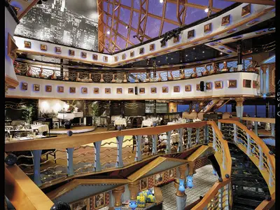 Mehrstöckiges Atrium der Carnival Miracle mit elegant gedeckten Tischen, Pianobühne, goldenen Balustraden. Blaue Lichtakzente im luxuriösen Innenraum.
