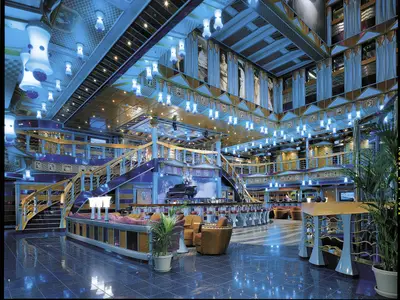 Ein luxuriöses, mehrgeschossiges Atrium der Carnival Miracle mit einer zentralen Bar, eleganten Sitzbereichen, geschwungenen Treppen und einer Vielzahl von leuchtenden Hängelampen in Blau und Goldtönen. Im Hintergrund sind auf hohen Wänden klassische Statuenmotive zu sehen.