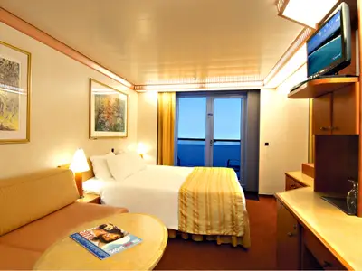 Eine helle Balkonkabine der Carnival Miracle mit einem gemachten Doppelbett, einem Ledersofa, zwei Bildern an der Wand, einem Fernseher und Glastüren zum Balkon mit Meerblick.