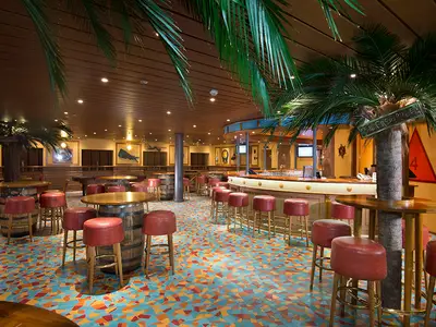 Eine leere Bar-Lounge auf der Carnival Miracle mit Palmen, bunten Fliesen, roten Barhockern und Holzmöbeln. Die warme Beleuchtung schafft eine einladende Atmosphäre.