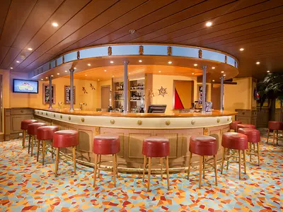 Blick in eine leere, runde Bar an Bord der Carnival Miracle. Rote Barhocker stehen vor der Holztheke. Der Boden ist ein Mosaikmuster in Blau, Orange und Rot.