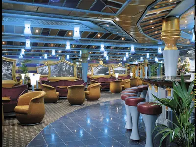 Luxuriöse Kreuzfahrt-Bar-Lounge. Blaue Lichtinstallationen, goldene Säulen, Schwarz-Weiß-Bilder und bequeme Sessel prägen den Raum. Eine lange Bar mit Hockern ist rechts zu sehen.