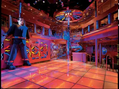 Thematischer Nachtclub auf der Carnival Miracle mit großer Frankenstein-Statue. Leuchtender Disco-Boden, Neon-Blitze und eine Wendeltreppe prägen den lebhaften Raum.