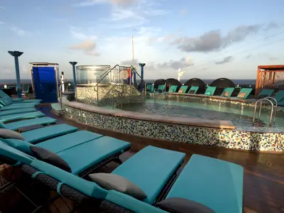 Blick auf den Poolbereich der Carnival Miracle mit Mosaikfliesen, türkisblauen Liegen und Rattanmöbeln, dem offenen Meer und Himmel im Hintergrund.