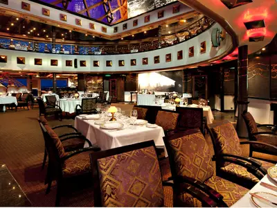 Elegantes, mehrstöckiges Restaurant auf der Carnival Miracle. Festlich gedeckte Tische, Stühle mit gemusterten Polstern. Obere Galerie mit goldenen Akzenten.
