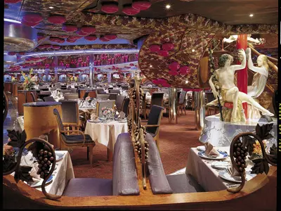 Großes, stilvolles Restaurant auf der Carnival Miracle. Die Tische sind gedeckt, und der Raum ist mit Weinreben, Skulpturen und roten Lichtelementen dekoriert.
