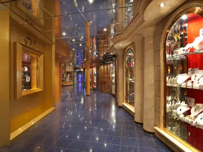 Elegante Einkaufsmeile auf der Carnival Miracle: glänzender blauer Boden, goldene Wände. Beleuchtete Schaufenster zeigen Schmuck und Kleidung. Spiegeldecke reflektiert Lichter.