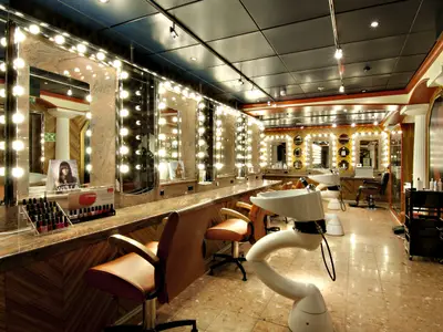 Ein heller Salon der Carnival Miracle mit mehreren Friseurstühlen und großen, beleuchteten Spiegeln. Links sind Nagelproduktstaender zu sehen, rechts Waschbecken. Der Boden ist gefliest.