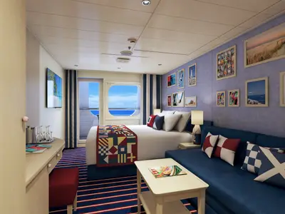 Eine helle Balkonkabine an Bord der Carnival Panorama, eingerichtet mit einem Doppelbett, Sofa, Schreibtisch und maritimer Dekoration. Ein Bullaugenfenster und eine Balkontür bieten Meerblick.