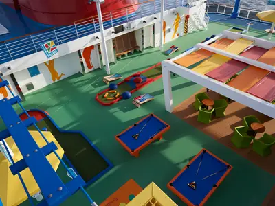 Ansicht von oben auf einen bunten Outdoor-Sportbereich auf der Carnival Panorama mit Minigolfbahn, Billardtischen und Lounge-Sitzgelegenheiten.