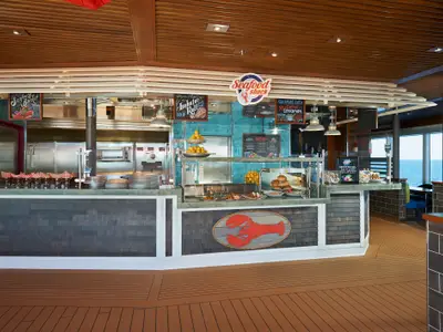 Ein helles und modern gestaltetes Spezialitätenrestaurant namens 'Seafood Shack' auf der Carnival Panorama mit einer Theke voller frischer Meeresfrüchte und einem weiten Blick auf das Meer durch große Fenster.