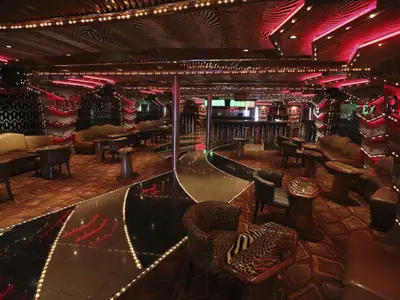 Blick in einen leeren Nachtclub an Bord der Carnival Paradise mit auffälligem Tierprint-Design, roter Neonbeleuchtung und einem zentralen, reflektierenden Weg.