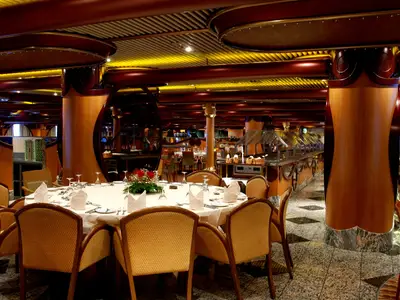 Eleganter Speisesaal auf der Carnival Paradise mit festlich gedeckten Tischen, Buffet und holzverzierten Säulen.