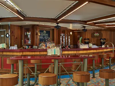 Innenansicht der RedFrog Pub Bar auf der Carnival Pride mit einer langen roten Theke, hohen Barhockern und Holzvertäfelung. Die Decke hat gemütliche Lichtinstallationen.
