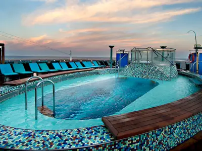 Geräumiges Pooldeck auf der Carnival Pride bei Sonnenuntergang. Ein großer Pool, ein Whirlpool, bequeme Liegen und das offene Meer im Hintergrund sind zu sehen. Die Beleuchtung ist sanft, der Himmel hat warme Farbtöne.