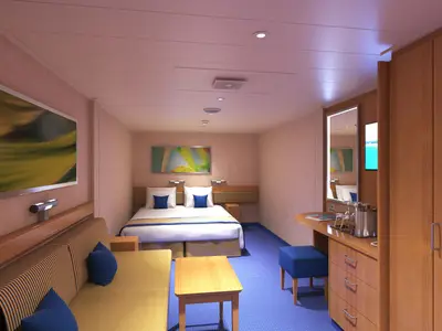 Innenansicht einer modernen Kabine der Carnival Radiance. Doppelbett mit blauen Kissen und hellblauem Teppich. Links ein gelbes Sofa und Holztisch. Holzmöbel, Spiegel und Kunstwerke an den Wänden.