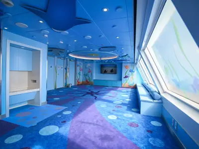 Blauer Kinderbereich auf der Carnival Radiance mit Unterwasser-Motiven. Oktopus-Teppich, animierte Fische auf großen Fensterflächen, Sitzbank, TV.