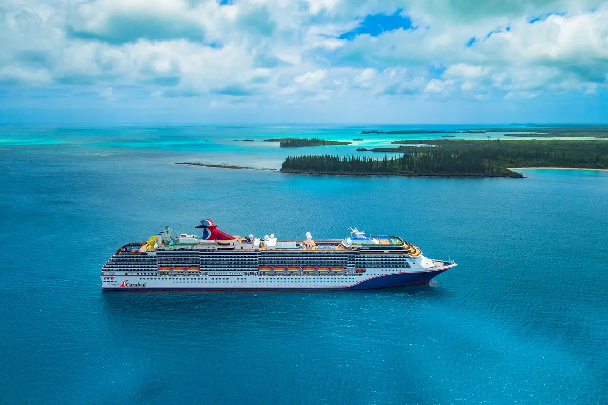 Die große Carnival Spirit auf türkisfarbenem Meer. Im Hintergrund grüne tropische Inseln unter blauem Himmel mit Wolken.