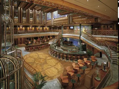 Detailreiche Gesamtansicht des luxuriösen Atriums der Carnival Spirit mit geschwungener Bar, Flügel und mehreren Lounge-Bereichen. Elegante Treppen und kunstvolle Deckenverzierungen sind sichtbar.