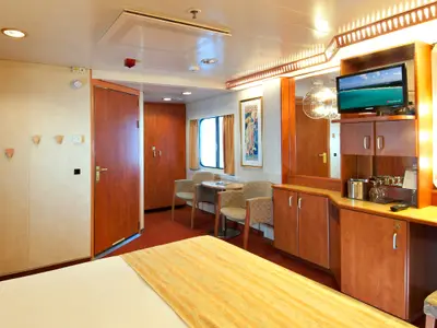 Gemütliche Außenkabine der Carnival Spirit mit Doppelbett, einem kleinen Sitzbereich mit Tisch und zwei Stühlen, und einem Unterhaltungsschrank mit Fernseher und Minibar.
