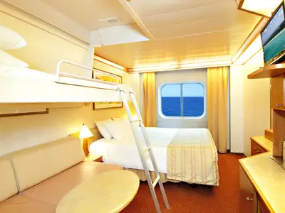 Eine helle Außenkabine auf der Carnival Spirit. Links ein Sofa und ein ausklappbares Etagenbett mit Leiter. Rechts ein Doppelbett und ein Fenster mit Blick auf das offene Meer.