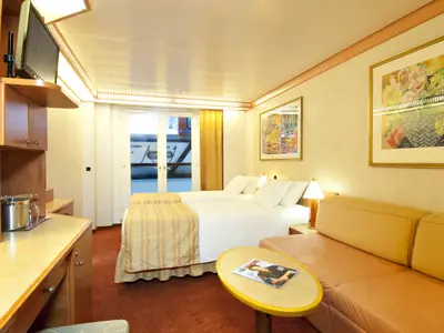 Helle Balkonkabine auf der Carnival Spirit. Zwei Einzelbetten, gelbes Sofa, Holzmöbel, Balkontür. Zeitschrift auf rundem Tisch.