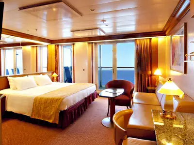 Luxuriöse Balkonkabine auf der Carnival Spirit. Großes Bett, Sitzbereich, Balkon mit Meerblick. Edle Einrichtung mit Holz, Lampen und Barbereich.
