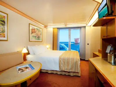 Blick in eine gut beleuchtete Balkonkabine der Carnival Spirit mit einem gemachten Doppelbett, einem kleinen Sofa, einem Fernseher und einer Balkontür, die auf das offene Meer führt.