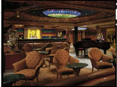 Blick in eine luxuriöse Schiffsbar mit kunstvollem Holzdekor, bunten Fliesen an der Bar, Grand Piano und gemütlichen Sesseln.