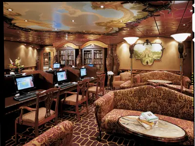Innenansicht einer luxuriösen Bibliothek an Bord der Carnival Spirit. Mehrere Computerarbeitsplätze und bequeme Sitzbereiche mit gemusterten Sofas sind zu sehen. Die Decke ist kunstvoll bemalt.