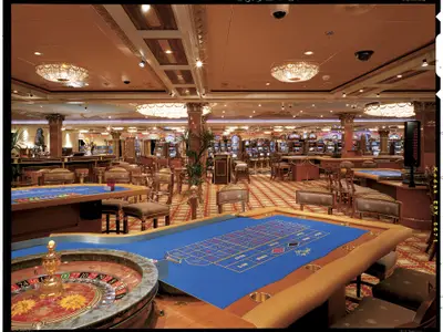 Casino auf der Carnival Spirit mit Roulette- und Blackjack-Tischen. Spielautomaten im Hintergrund. Luxuriöser Innenraum mit Kronleuchtern und verzierten Säulen.