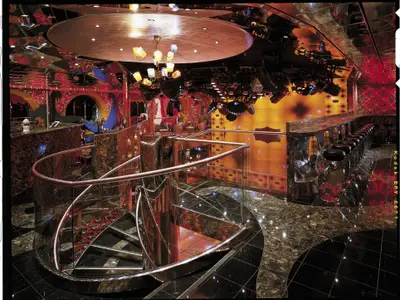Blick in einen glänzenden Nachtclub auf der Carnival Spirit mit einer Wendeltreppe, Barhockern und bunten Lichtern, ohne Personen.