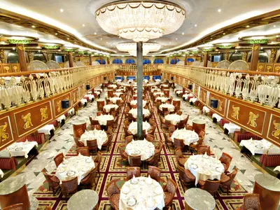 Ein luxuriöses Restaurant auf der Carnival Spirit, festlich gedeckte Tische, goldene Geländer, opulente Kronleuchter.